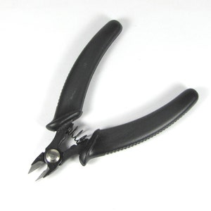 May include: Black wire cutters with textured, curved handles. The cutting blades are silver and connected by a spring. The handles are made of a matte black material. The tool is designed for precision cutting.