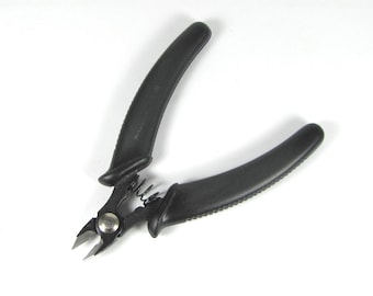 May include: Black wire cutters with textured, curved handles. The cutting blades are silver and connected by a spring. The handles are made of a matte black material. The tool is designed for precision cutting.