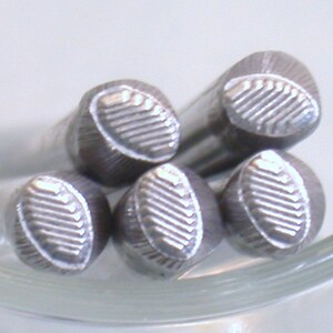 May include: Five silver metal stamp heads with a textured oval design. The stamp heads are arranged in a circle.