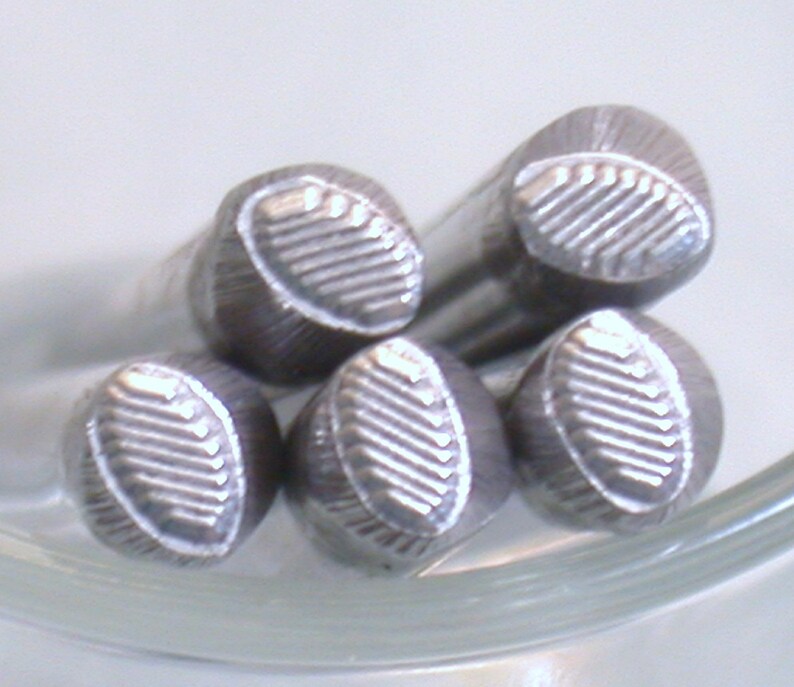 May include: Five silver metal stamp heads with a textured oval design. The stamp heads are arranged in a circle.
