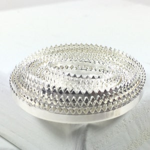 May include: A set of silver metal trim with a scalloped edge. The trim is stacked in a circle.