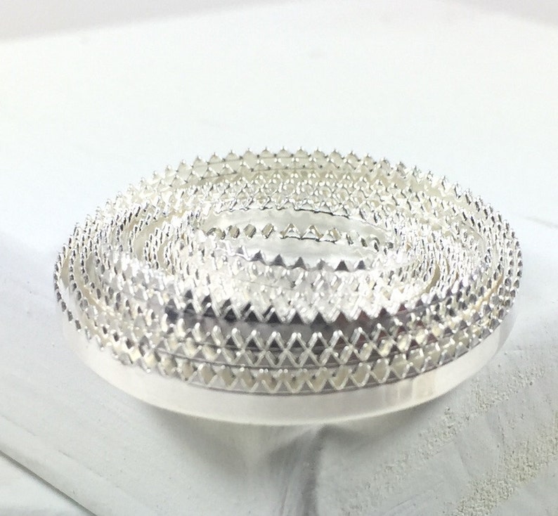 May include: A set of silver metal trim with a scalloped edge. The trim is stacked in a circle.