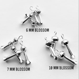 May include: Silver metal flower-shaped bead caps in three sizes: 6 mm, 7 mm, and 10 mm. The caps have a small loop at the top for attaching to jewelry.