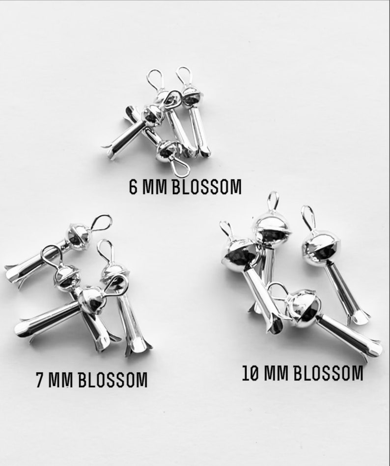 May include: Silver metal flower-shaped bead caps in three sizes: 6 mm, 7 mm, and 10 mm. The caps have a small loop at the top for attaching to jewelry.
