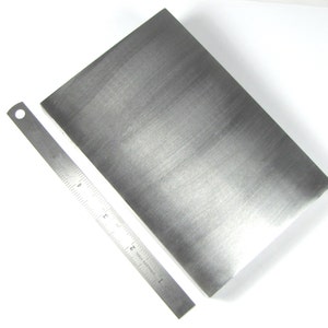 May include: A brushed silver metal rectangle with a ruler for scale. The rectangle is approximately 6 inches long and 4 inches wide.