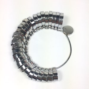 May include: A silver ring sizer with a series of numbered rings, ranging from size 2 to size 13. The rings are attached to a metal band.