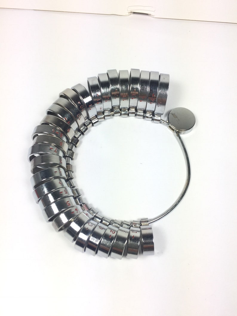 May include: A silver ring sizer with a series of numbered rings, ranging from size 2 to size 13. The rings are attached to a metal band.