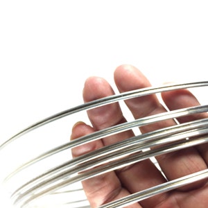 May include: A close-up of a bundle of silver wire, showing the smooth, shiny surface of the wire. The wire is coiled and held in a hand.