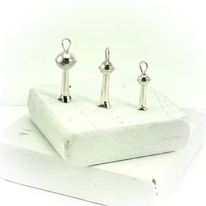 May include: Three silver pendant charms in the shape of a stylized tower with a round top. The charms are arranged in order of size, with the largest charm on the left and the smallest charm on the right.