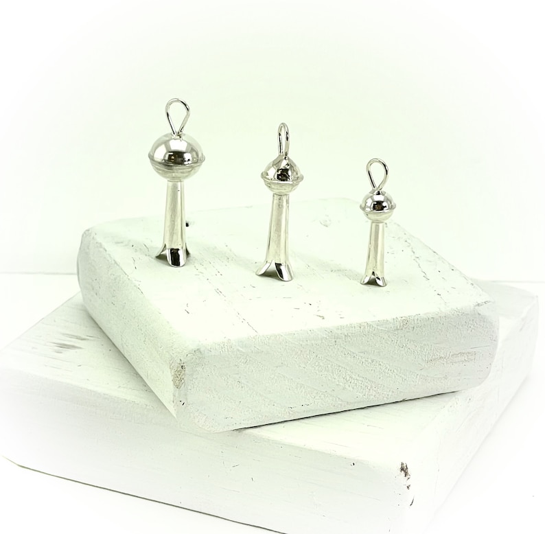 May include: Three silver pendant charms in the shape of a stylized tower with a round top. The charms are arranged in order of size, with the largest charm on the left and the smallest charm on the right.