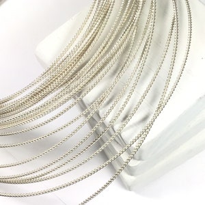 May include: A close-up of a bundle of silver-colored wire, arranged in a fan shape. The wire is thin and has a delicate, textured surface.