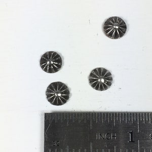 May include: Four silver metal buttons with a starburst design, measured against a ruler with inch markings.