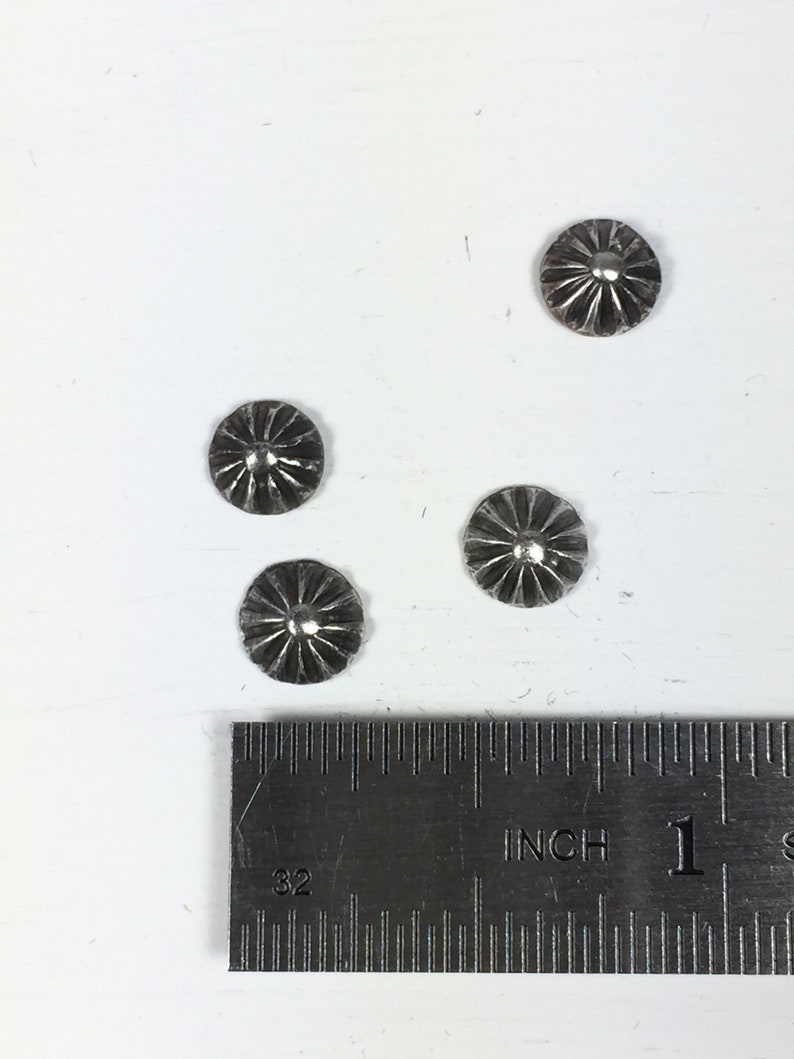May include: Four silver metal buttons with a starburst design, measured against a ruler with inch markings.