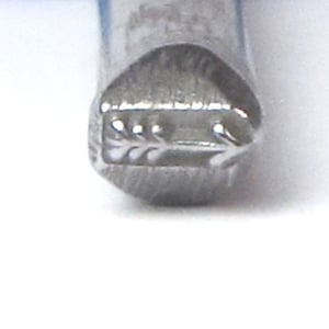 May include: Close-up of a silver metal stamp with a design of a stylized leaf and arrow.