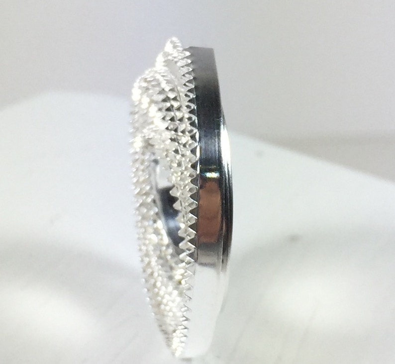 May include: A silver ring with a detailed, intricate design. The ring is a wide band with a textured surface.