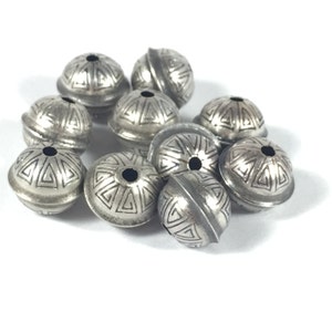 May include: A group of silver-toned metal beads with a geometric design. The beads are round and have a hole in the center for stringing.