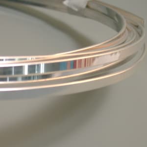 May include: Close-up of silver metal trim, showing the shiny, reflective surface of the metal. The trim is rolled up in a coil.