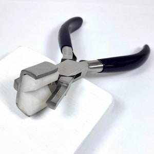 May include: A pair of metal pliers with dark blue handles and a white, angled jaw. The pliers are designed for jewelry making or crafting, with a focus on precision and detail work. The tool is set against a white background.