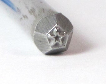 May include: Close-up of a silver metal stamp with a five-pointed star design. The stamp is hexagonal in shape.
