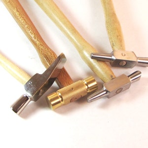 May include: A collection of small hammers with wooden handles and metal heads. The hammer heads have various shapes, including flat, rounded, and angled. The handles are light brown, and the metal heads are silver and gold.