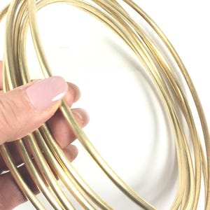May include: A bundle of thin, golden-colored metal hoops, held in a person's hand. The hoops are tightly coiled, creating a circular shape. The metal has a smooth, reflective surface, and the overall appearance is bright and shiny.