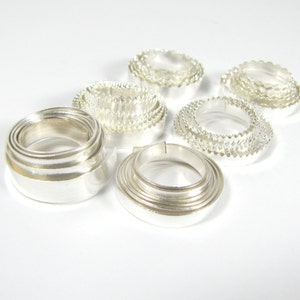 May include: A set of silver metal rings, some are stacked and some are single, all are smooth and shiny.