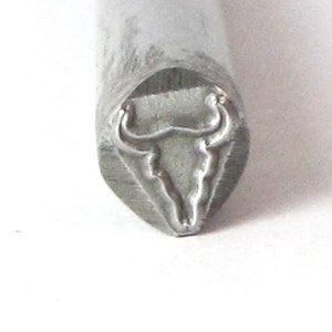 May include: A silver metal stamp with a design of a bull's head. The stamp is used for creating impressions in metal.