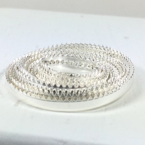 May include: A set of silver rings with a decorative, scalloped edge. The rings are stacked on top of each other, creating a spiral effect.