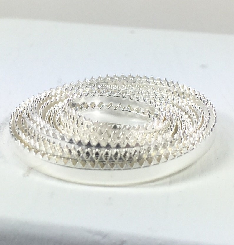 May include: A set of silver rings with a decorative, scalloped edge. The rings are stacked on top of each other, creating a spiral effect.