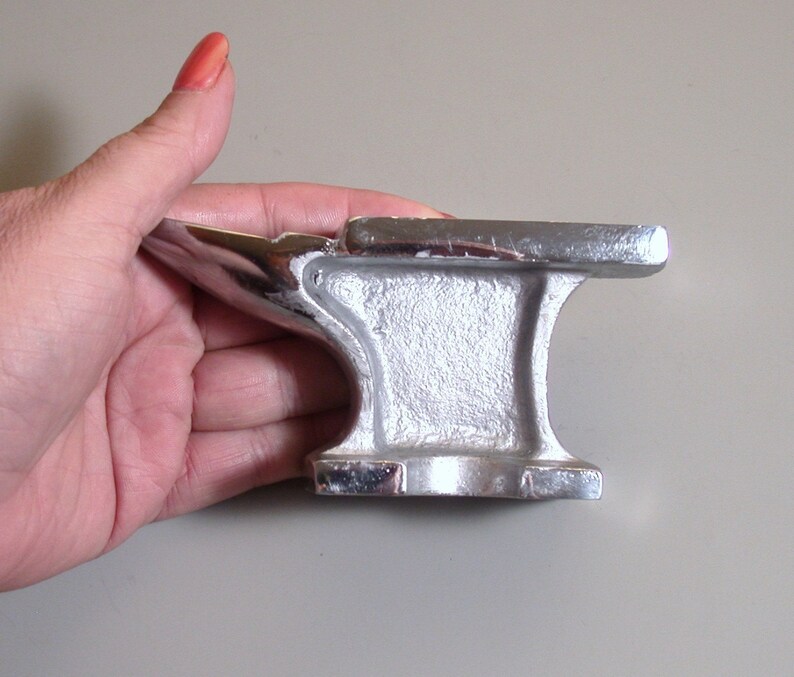 May include: A small, silver-colored metal anvil with a rounded top and a flat base. The anvil is about 4 inches tall and 3 inches wide.