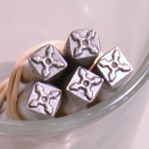 K&ouml;nnte beinhalten: F&uuml;nf silberne Metallstempel mit einem vierzackigen Sternmuster. Die Stempel sind in einem Stapel angeordnet, wobei die Spitzen der Sterne nach au&szlig;en zeigen.