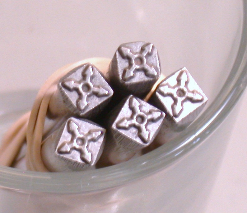 K&ouml;nnte beinhalten: F&uuml;nf silberne Metallstempel mit einem vierzackigen Sternmuster. Die Stempel sind in einem Stapel angeordnet, wobei die Spitzen der Sterne nach au&szlig;en zeigen.