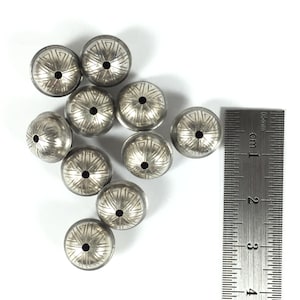 Puede incluir: Diez cuentas de metal plateadas con un patr&oacute;n decorativo. Las cuentas miden aproximadamente 1 cm de di&aacute;metro y tienen un peque&ntilde;o agujero en el centro.