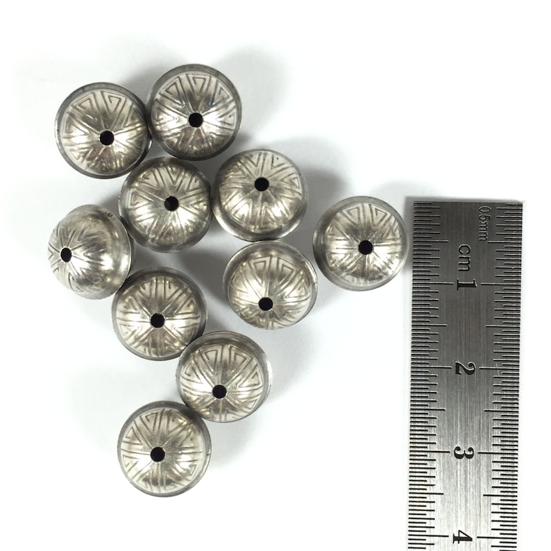 Puede incluir: Diez cuentas de metal plateadas con un patr&oacute;n decorativo. Las cuentas miden aproximadamente 1 cm de di&aacute;metro y tienen un peque&ntilde;o agujero en el centro.