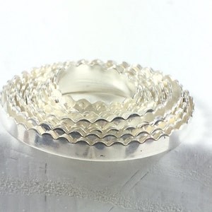 May include: A set of silver-colored, scalloped-edge cookie cutters stacked on top of each other.
