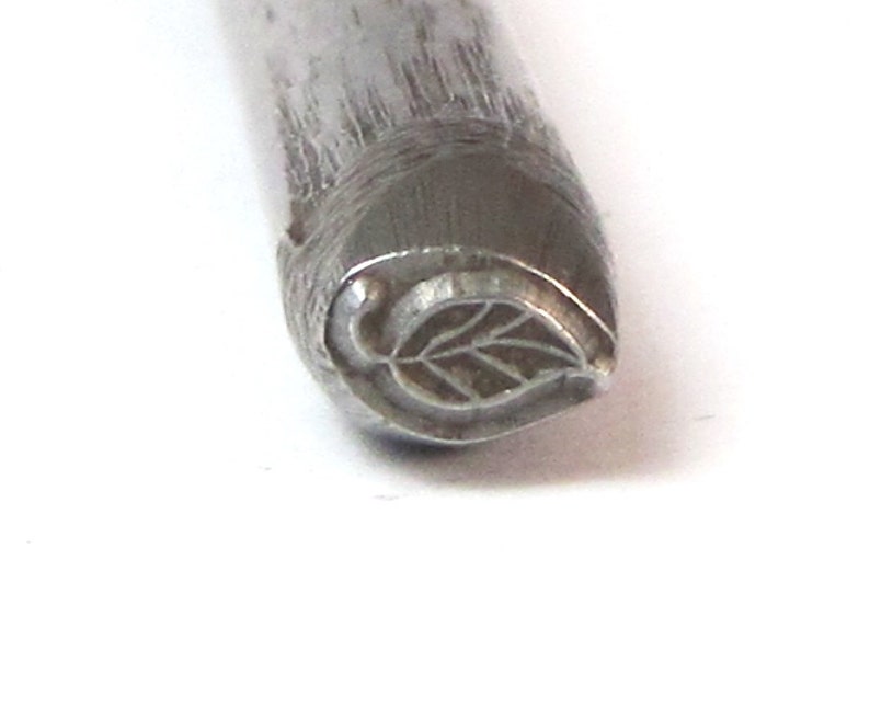 May include: Close-up of a metal leaf-shaped stamp for crafting and jewelry making.