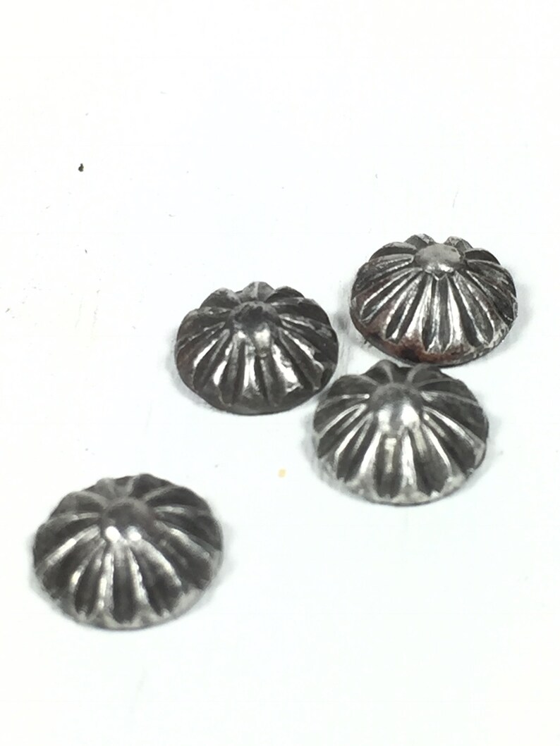 May include: Four silver metal dome-shaped buttons with a decorative, radial pattern. The buttons have a slightly aged, tarnished look.