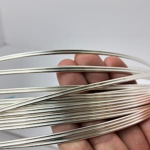 May include: A close-up of a coil of silver wire. The wire is shiny and smooth, and it is coiled in a tight spiral.