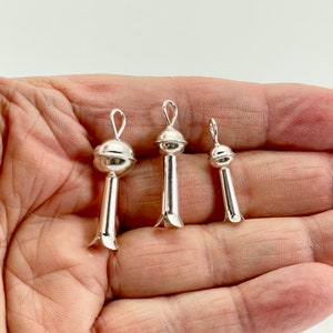 May include: Three silver pendant charms in the shape of a stylized flower with a round top. The charms are different sizes and are shown in a hand.