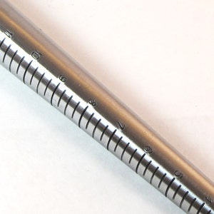 May include: A silver ring sizer with markings from size 4 to size 13.