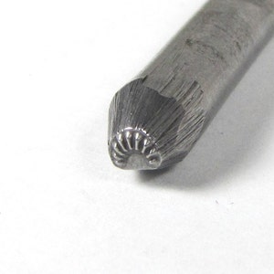 May include: A close-up of a metal stamping tool with a decorative design. The tool is silver in color and has a rounded tip.