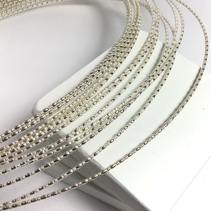 Puede incluir: Alambre de abalorios plateado, un carrete de alambre plateado con pequeñas cuentas, perfecto para la elaboración de joyas.