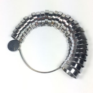 May include: A silver ring sizer with numbered rings from 1 to 17. The rings are attached to a metal loop.