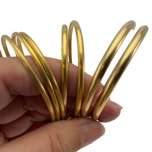 May include: A set of six gold-colored metal rings, stacked and held in a hand. The rings are smooth and shiny, with a slightly rounded edge.