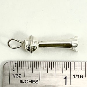 May include: A silver pendant with a round bead and a long, thin stem ending in a flower-shaped tip. The pendant is about 1 inch long and is measured against a ruler.