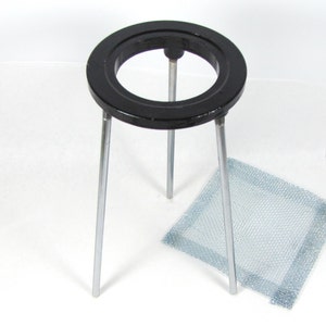 May include: A black metal ring stand with three legs and a wire mesh. The stand is used to support beakers and other laboratory equipment.