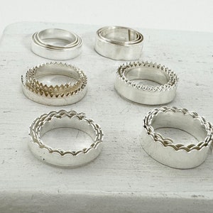 May include: Set of six silver rings with different decorative edges. The rings are stacked in pairs, with each pair having a different design.