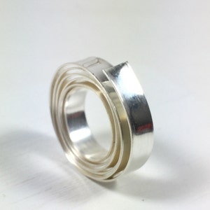 May include: A silver ring made of multiple thin bands of metal that are twisted together to form a spiral shape.