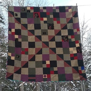 May include: A patchwork quilt with a variety of colors and patterns, including black, red, green, and purple. The quilt is made up of squares and triangles, and it is hanging on a clothesline.