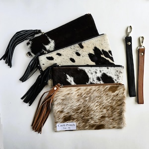May include: Four cowhide pouches in black and white, and tan and white patterns, with matching leather tassels and wrist straps. One pouch has a label that reads "Cacti Pouch Tan-04".